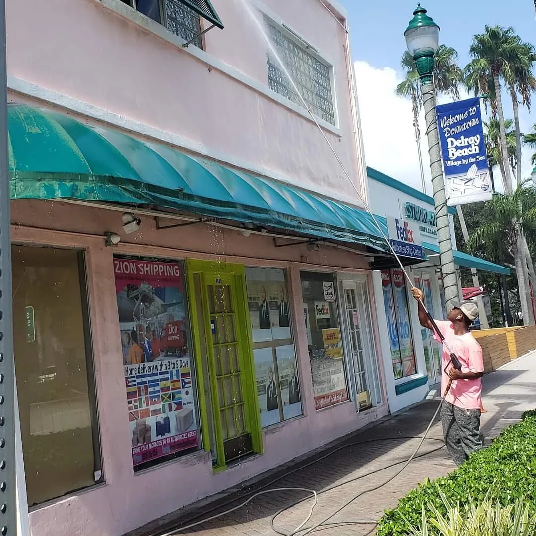 A Magic Touch crew member washing a storefront under a Delray Beach sign